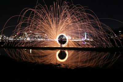 Person making light painting with reflection in lake against sky