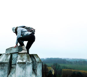 Side view of man standing on rock against clear sky