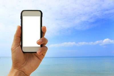 Close-up of hand holding mobile phone against sea