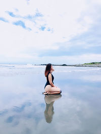 Woman sitting in sea against sky