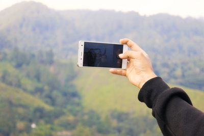 Midsection of man using mobile phone against mountain