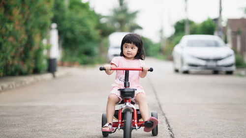 Portrait of cute boy riding toy car on road in city