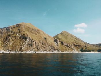 Scenic view of sea by mountain against sky