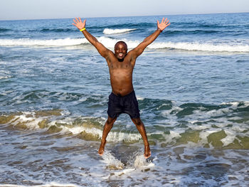 Full length portrait of shirtless man jumping at beach