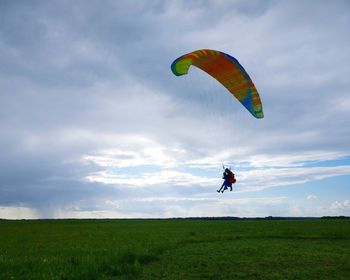People paragliding over field against cloudy sky