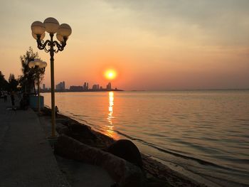 Street light by sea against sky during sunset