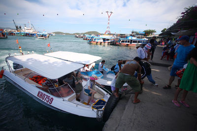 People on boats moored at harbor against sky