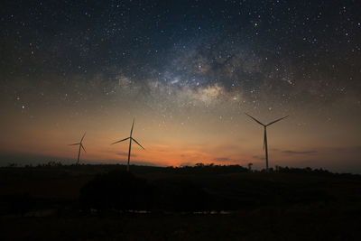 Silhouette wind turbines on field against sky at night