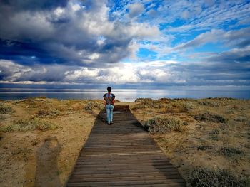 Rear view of woman on footpath at field against sea