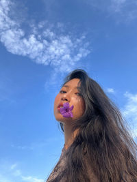 Low angle view of young woman looking away against sky