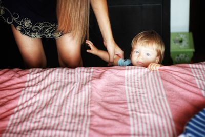 Portrait of cute boy withe blonde hair and midsection of woman sitting near bed at home 