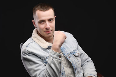 Portrait of young man standing against black background