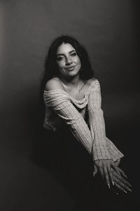 Portrait of young woman standing against black background