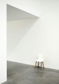 Empty chair on floor against white wall