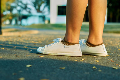 Low section of woman wearing white canvas shoes standing on road