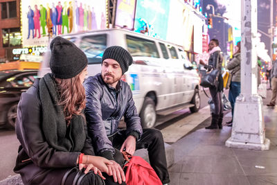 Couple looking each other face to face while sitting on city street at night