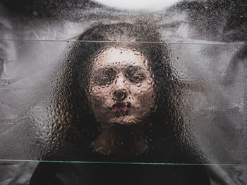Close-up portrait of woman seen through glass window