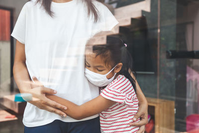 Girl embracing mother while standing by glass