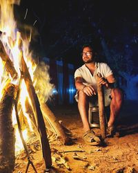 Portrait of young man sitting on bonfire at night