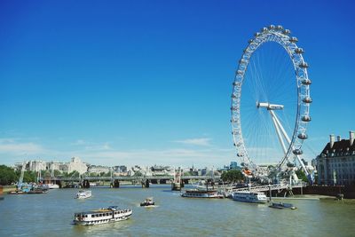 London eye by thames river against blue sky