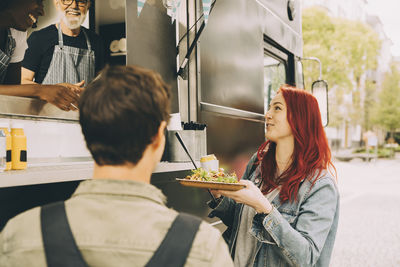 Smiling customer talking to owner while standing with food plate on street