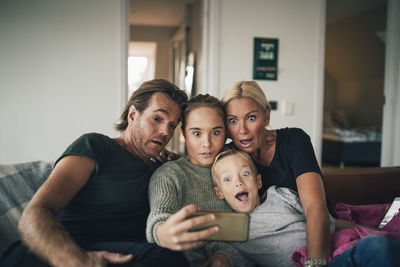 Shocked family taking selfie through smart phone while sitting on sofa at home
