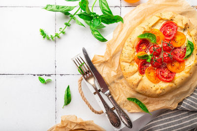 Fresh homemade galette with tomatoes, ricotta cheese and basil on white tile background. top view.