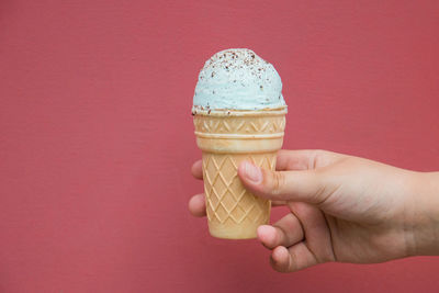 Close-up of hand holding ice cream against red background