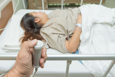 Cropped hand holding medical equipment against female patient sleeping on bed