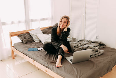 Young woman using phone while sitting on laptop