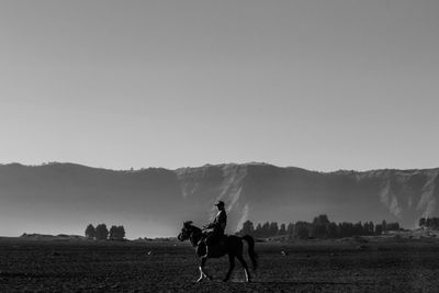 Silhouette man riding horse on field against sky