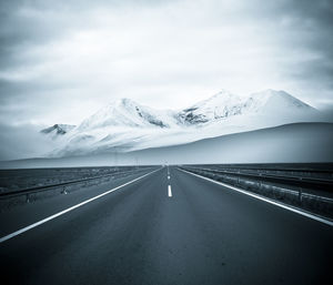 Road leading towards snowcapped mountains against sky