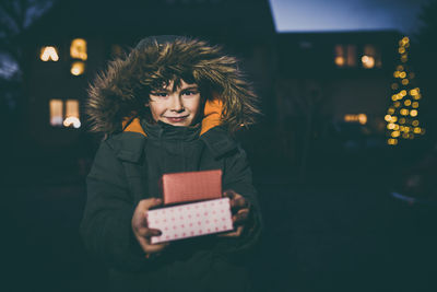 Portrait of smiling young woman holding box at night