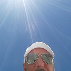 Low angle view of man in sunglasses against blue sky on sunny day