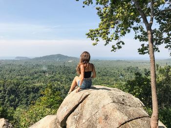 Rear view of woman sitting on rock against forest
