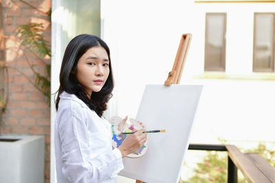 Young woman holding colorful palate by canvas 