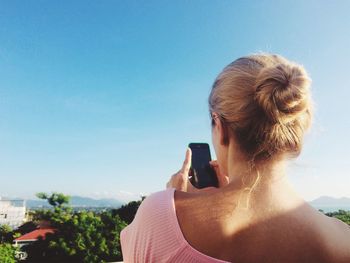 Woman using mobile phone against clear blue sky