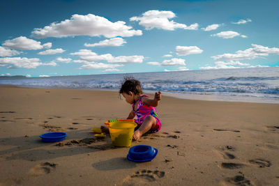 Baby girl sitting on beach by sea against sky