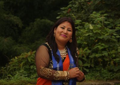 Portrait of smiling mid adult woman in sari standing against plants