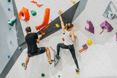 Back view of sportive couple in activewear climbing artificial wall with colorful grips during training together in light modern gym