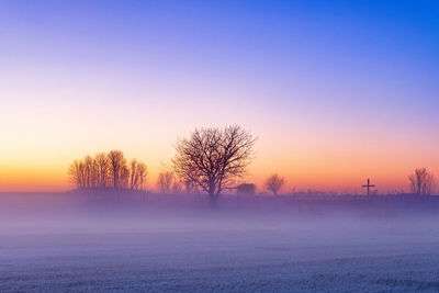 Misty morning in winter with a religious cross and trees in silhouette