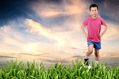 Full length portrait of boy with soccer ball standing on field against sky