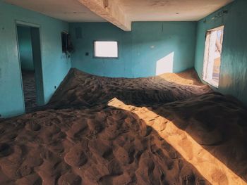 Interior of abandoned house with sand dune taking over and sun going through the door.