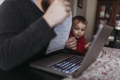 Close up of young son looking at dads computer while he works at home