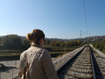 Rear view of man standing on railroad track against clear sky