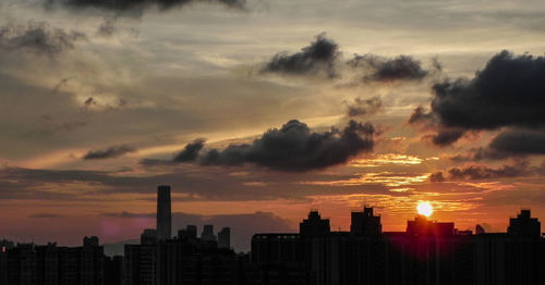 Silhouette of city against cloudy sky during sunset