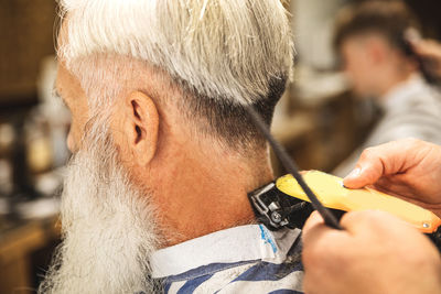 Hairdresser cutting hair of customer through electric razor in salon