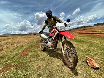 Woman with motorcycle standing on field against cloudy sky