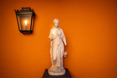 Statue of illuminated lamp against orange wall