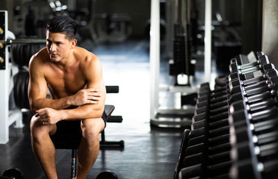 Shirtless man looking away while sitting in gym